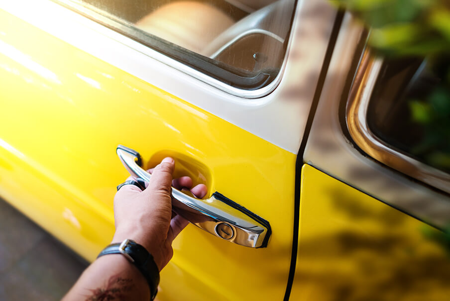 Ateliê do carro: mão masculina com relógio no pulso segurando a maçaneta de um carro antigo  amarelo e branco.
