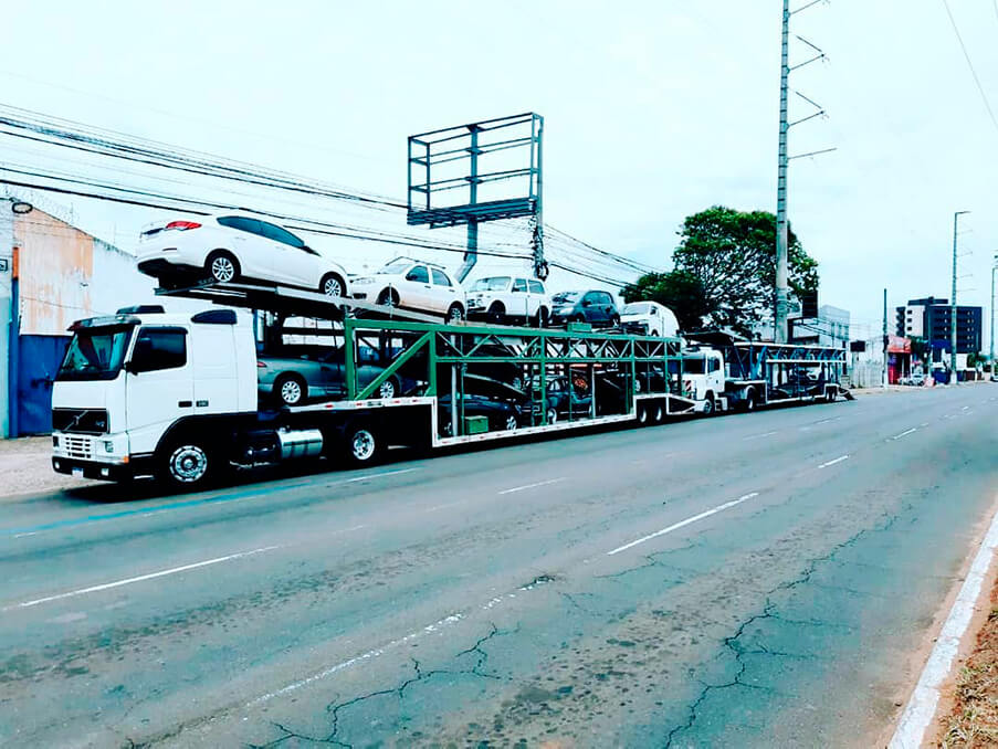 Dois caminhões cegonhas de transporte de veículos carregados com carros, estacionados em uma rua